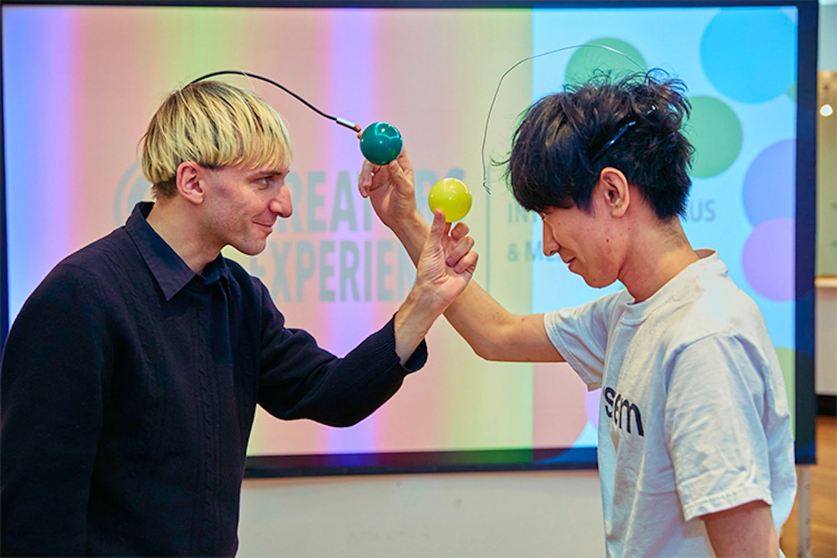 展示会場で、ニール・ハービソン氏（左）と制作者の與座（右）が色のボールを重ね合わせている様子